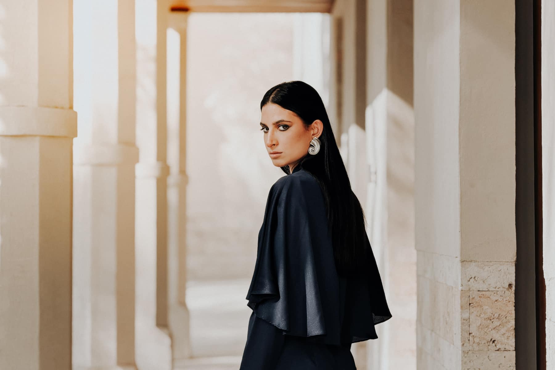 Model turning to camera in a sunlit colonnade