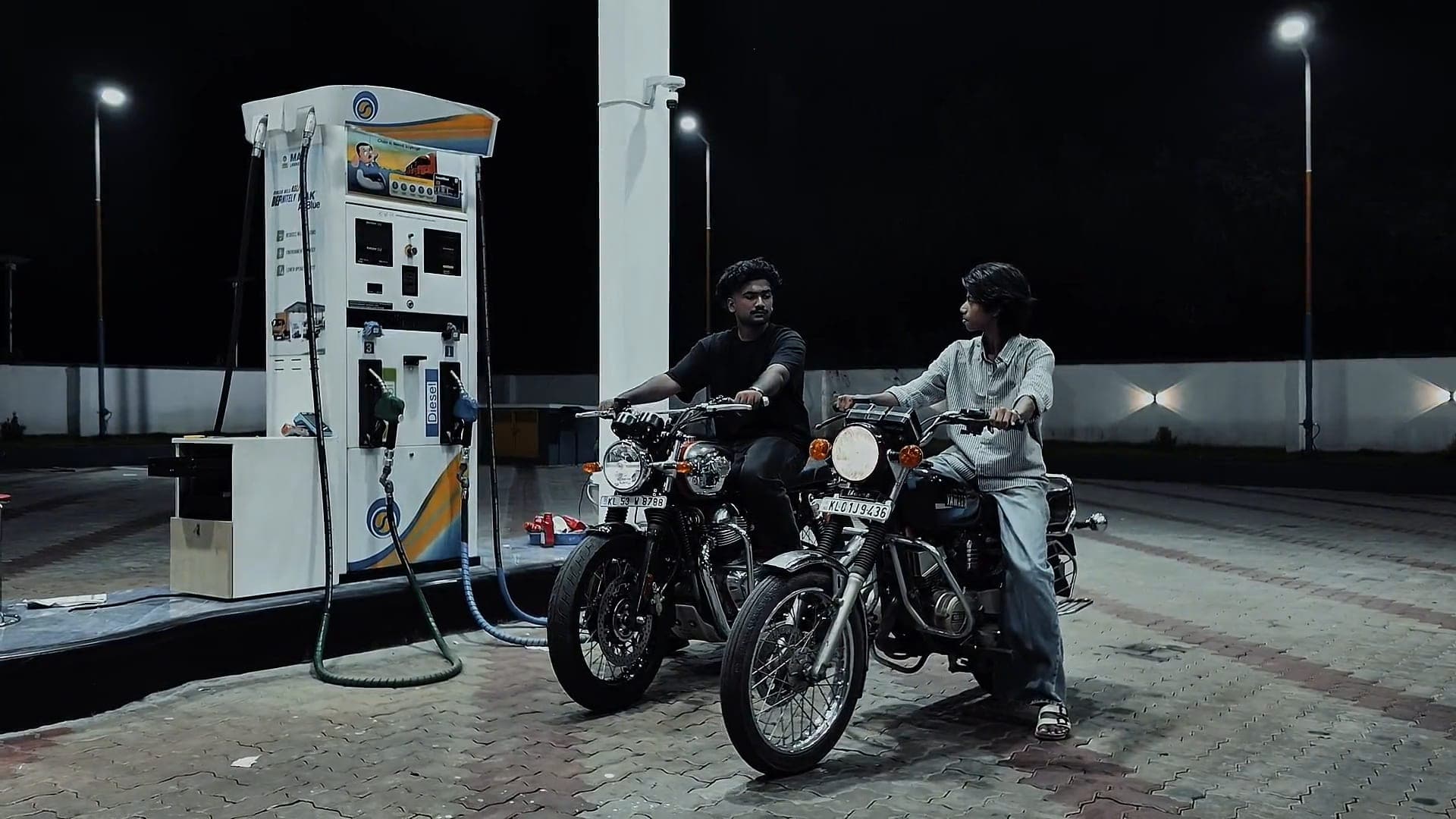 Two riders at a petrol station forecourt at night